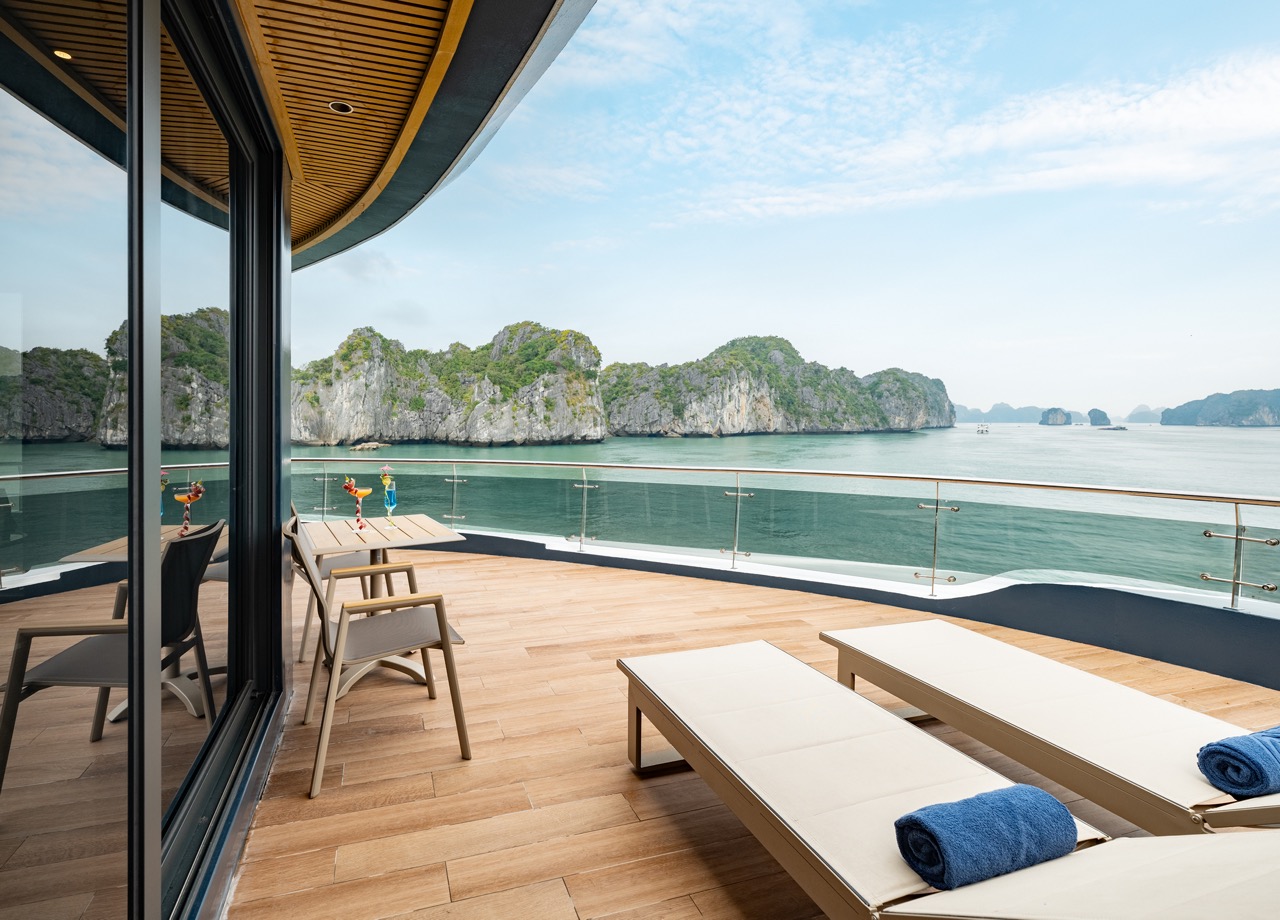Sunlit yacht deck with beige lounge chairs, a small table with colorful cocktails, and a glass railing overlooking turquoise water and distant rocky islands.” (informative)