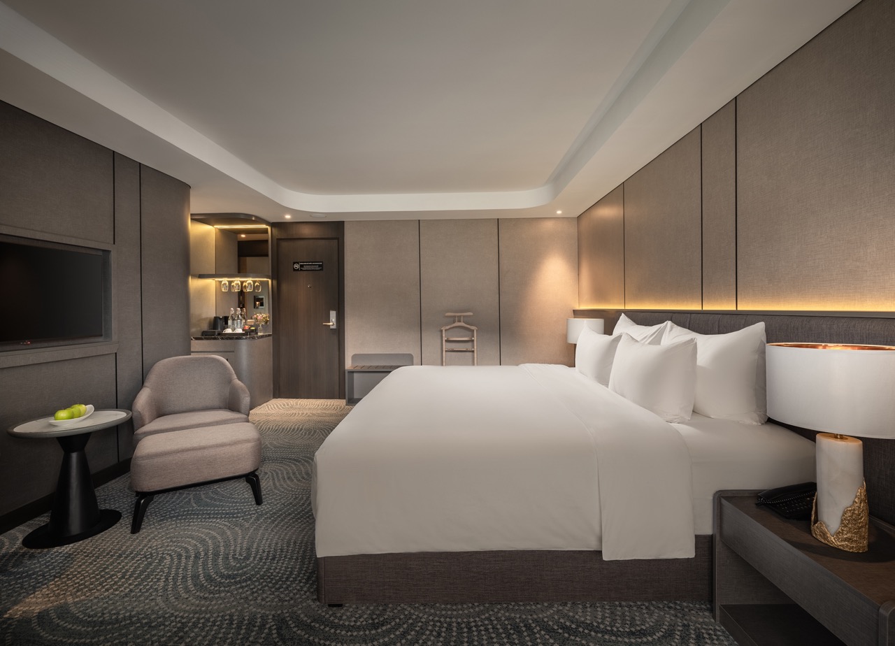 Modern hotel room with a king bed, gray upholstered headboard, and warm ambient lighting.