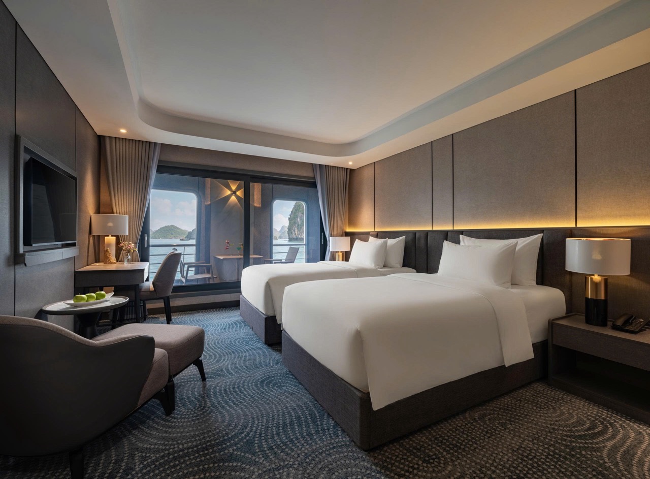 Hotel room with two double beds, sea view balcony, and seating area by a large window; warm lighting and modern decor.