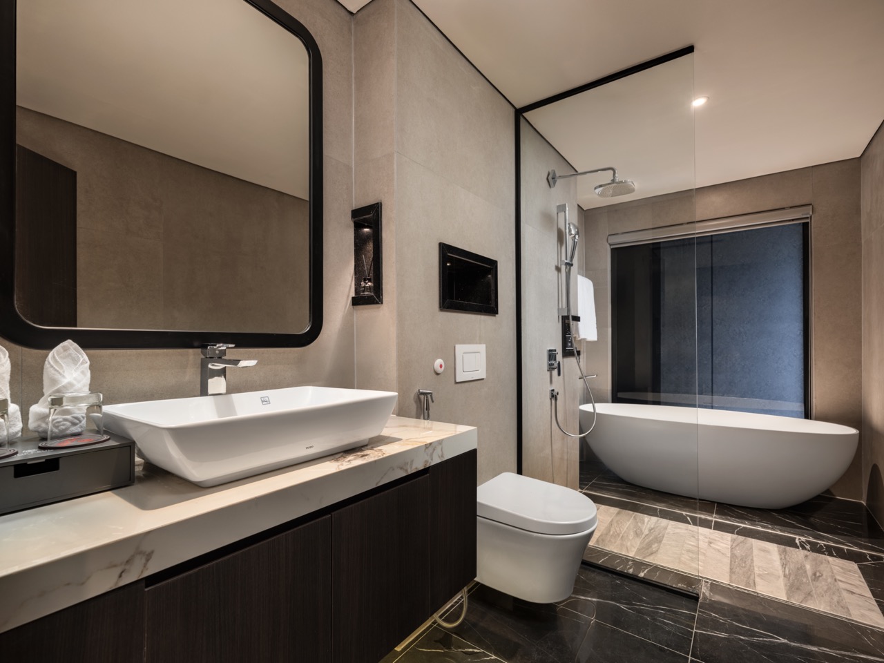 Modern bathroom with a white vessel sink on a marble countertop, dark wood vanity, and a large black-framed mirror.