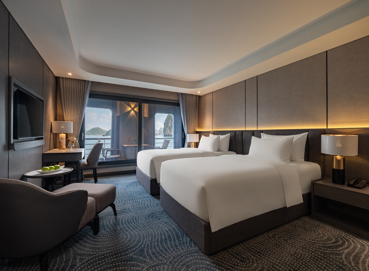 Two queen beds in a modern hotel room with a balcony and an ocean view outside the glass doors