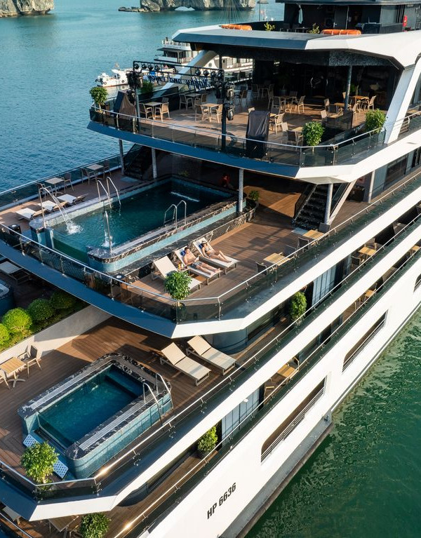 A large multi-deck luxury yacht with swimming pools and sun loungers on each level, afloat on calm blue water.