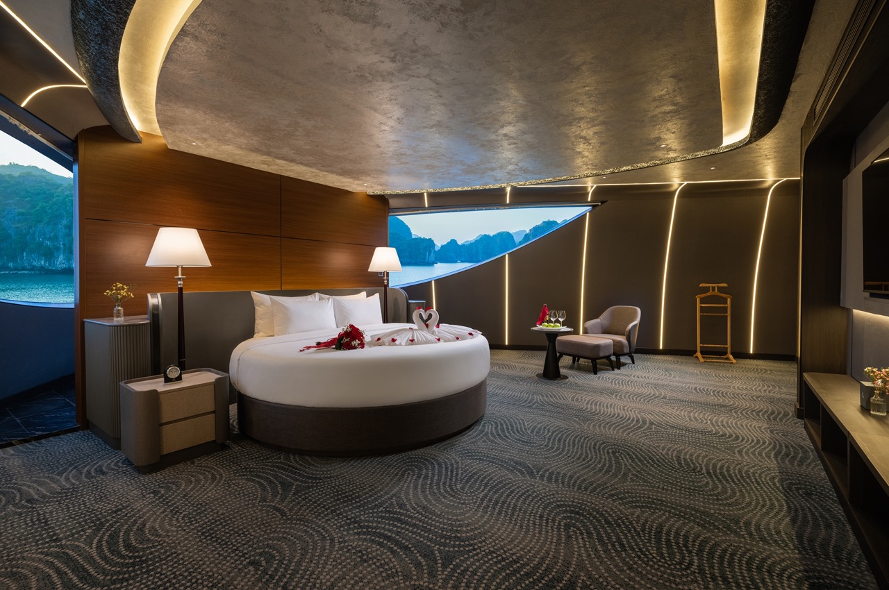 Luxurious hotel bedroom with a round bed, rose petals, and towel swans, near a panoramic sea view.