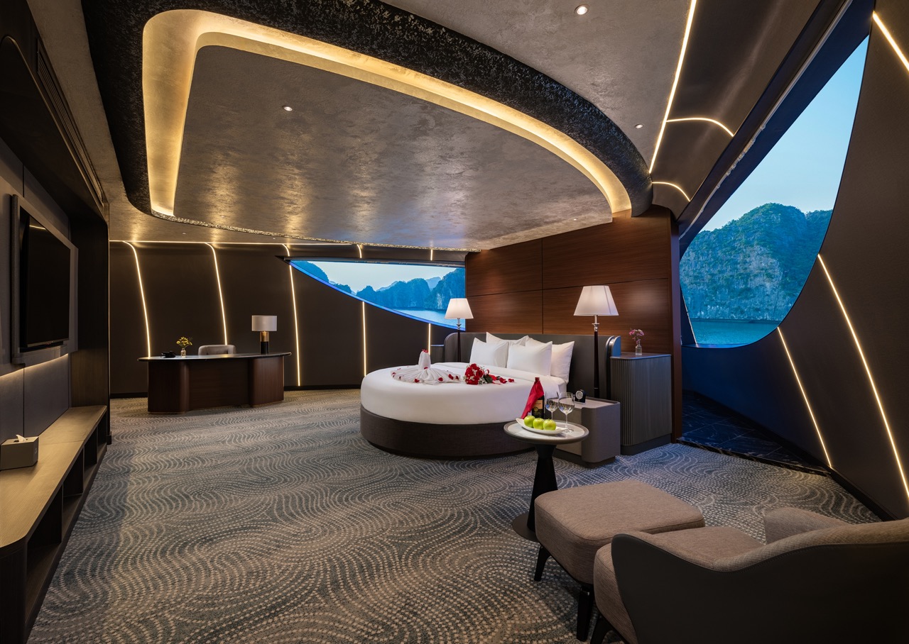 Luxurious hotel suite on a yacht with a round bed, modern lighting, and sea view through curved windows; mountains in distance