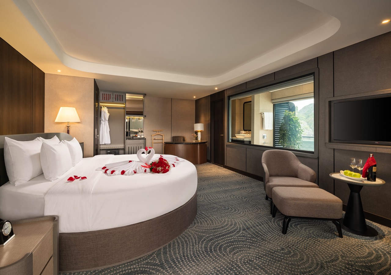 Romantic hotel room with a round bed, towel swans, and rose petals on white linens.