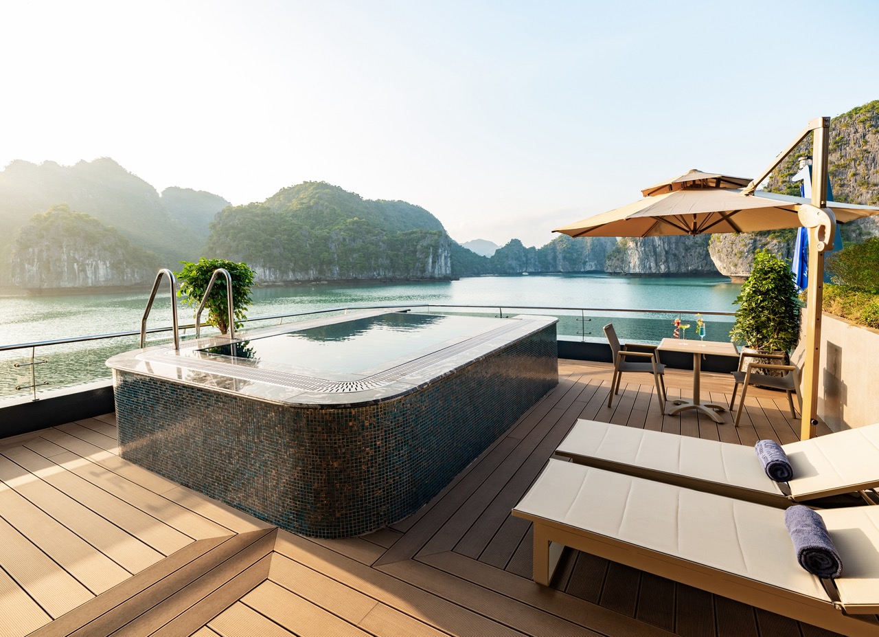 Luxurious rooftop terrace with a tiled-jacuzzi overlooking calm turquoise water and limestone cliffs, under a bright sky.