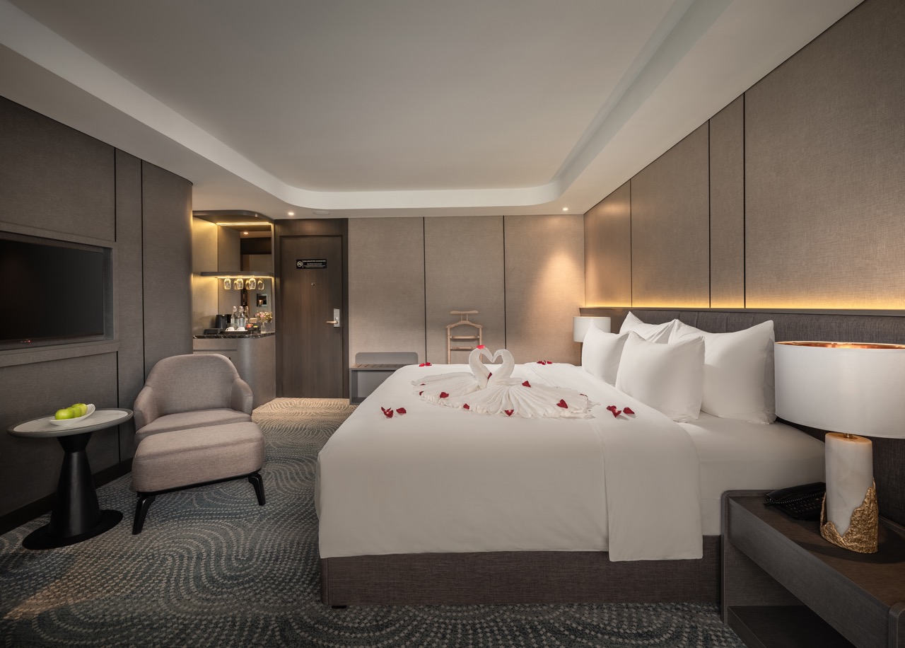 Luxurious hotel room with a king bed, towel swans and rose petals on the duvet, and soft ambient lighting.