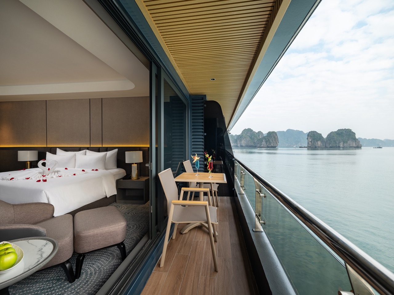 Balcony suite with a sea view: small dining table for two, two chairs, and a bed visible inside the hotel room.
