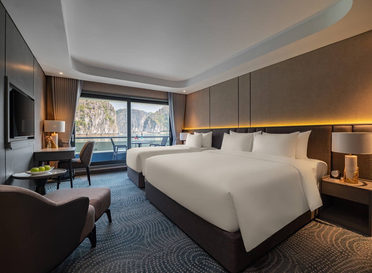 Luxurious hotel room with two white beds, sitting area, and a balcony overlooking rocky cliffs and water nearby coastal scenery