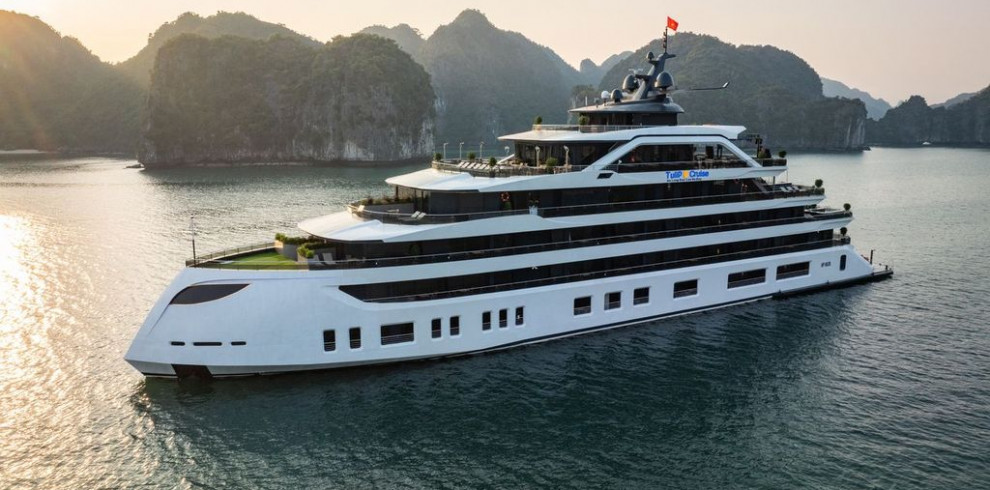 White luxury cruise yacht with multiple decks sailing in a calm bay at sunset, limestone cliffs in the background