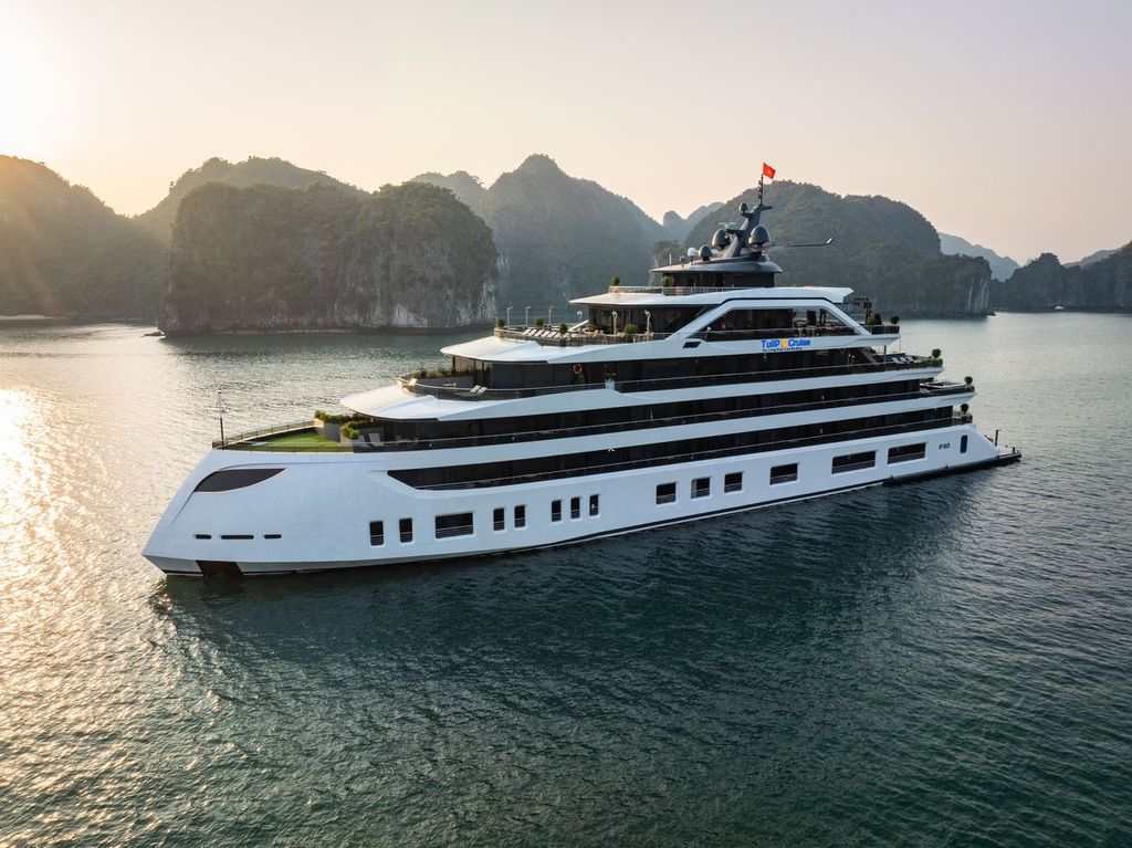 White luxury cruise yacht with multiple decks sailing in a calm bay at sunset, limestone cliffs in the background
