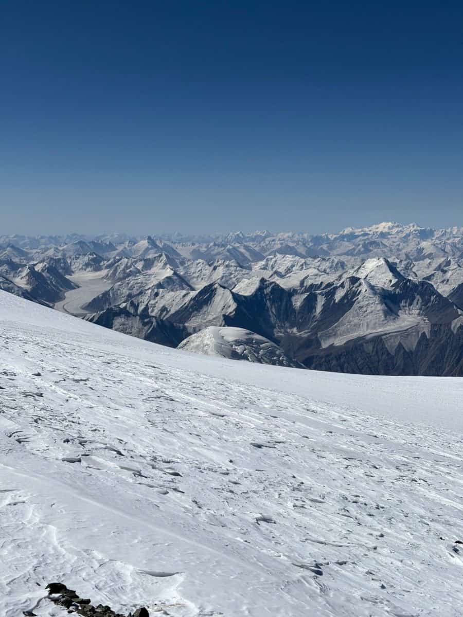 Snow-covered mountains stretch far into the distance under a clear blue sky, showcasing a stunning, pristine winter landscape.