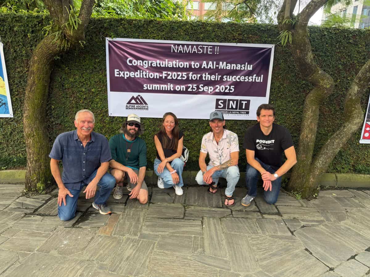 Five individuals pose together in front of a congratulatory banner for a successful mountaineering expedition.