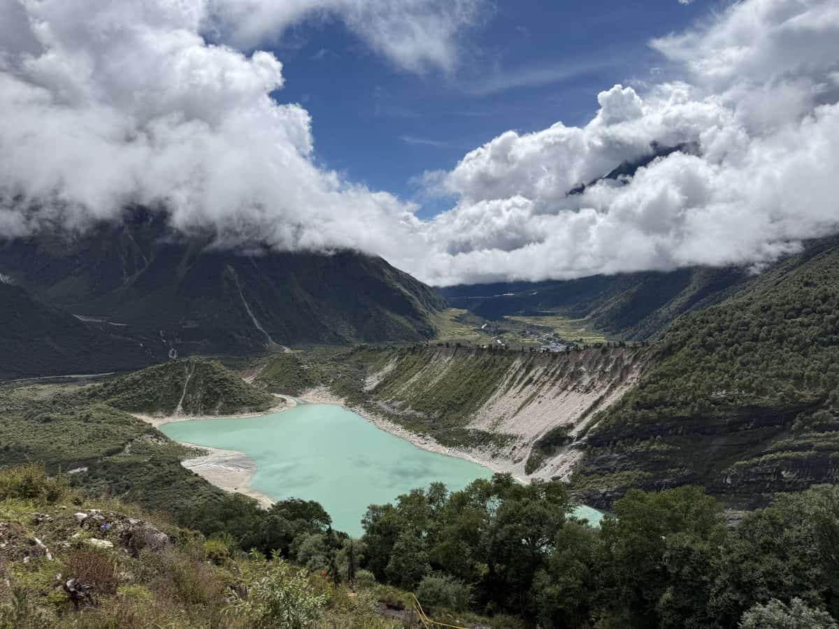 A turquoise lake surrounded by mountains and greenery under a cloudy sky.