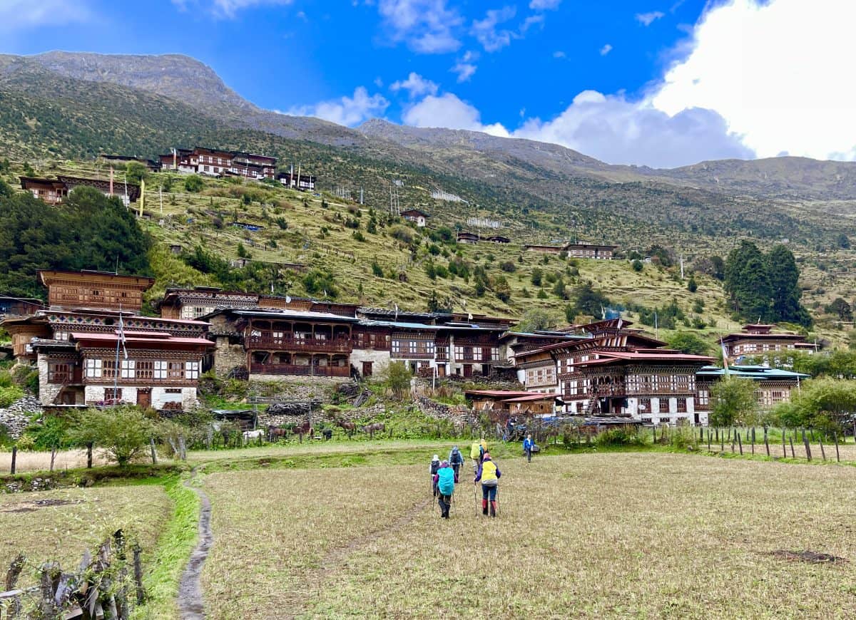 Scenic view of traditional Bhutanese buildings on a hillside, with people walking in a grassy field under a clear blue sky.