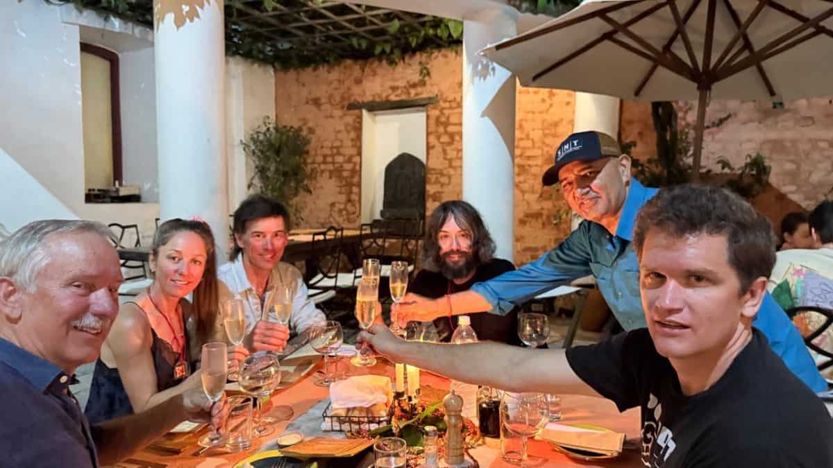 A group of six people at a dinner table celebrating with raised glasses in a warm, inviting atmosphere.