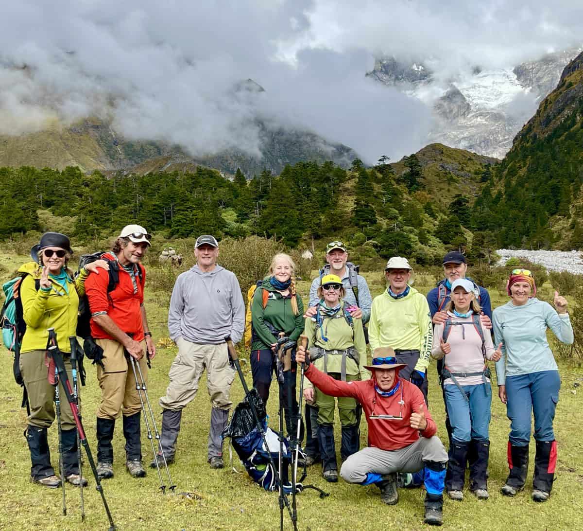 A group of hikers stands together in a mountainous landscape, surrounded by greenery and clouds, showcasing a sense of adventure and camaraderie.