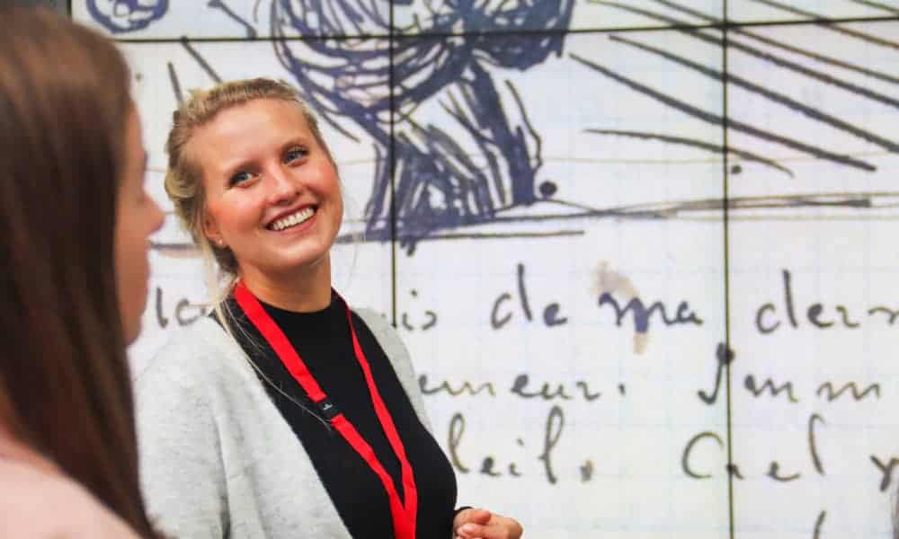 Woman smiling and looking at friend. Colourful wall in background.