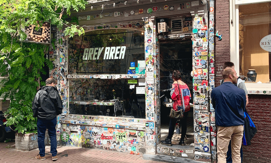 Menschen warten vor dem mit Stickern beklebten Grey Area Coffeeshop.