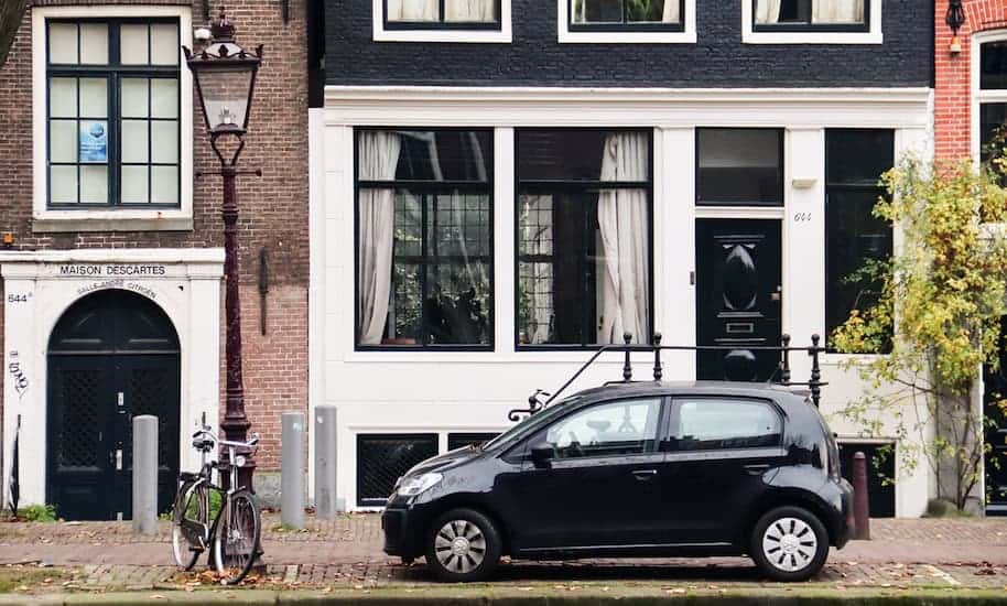 Schwarzes Auto parkt vor einem schwarz weißen Grachtenhaus
