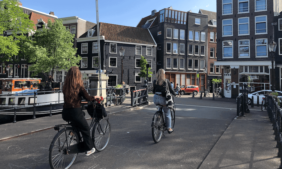 Zwei Frauen radeln über eine Brücke in Amsterdam