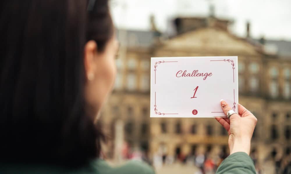 A woman holding a white card with a challenge written on it. The card reads 'Challenge 1'.