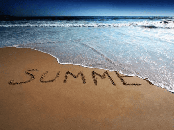 The word "SUMMER" is written in the sand on a beach, with sea waves approaching and a clear blue sky in the background.