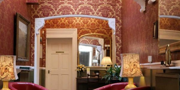 An ornately decorated hallway with red chairs and a mirror.
