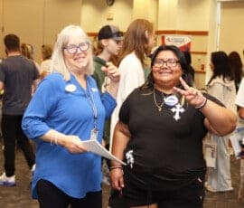 Two women, one older one younger, smiling. The younger woman giving a peace sign