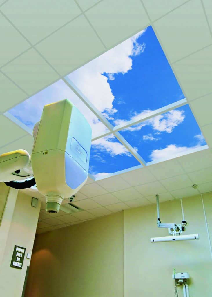 Square window showing a bright blue sky with clouds in a room above an MRI machine.