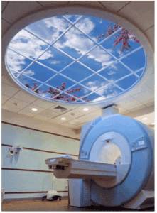 MRI procedure room with a circular window in the ceiling showing a blue sky with a few clouds and flowering tree branches.