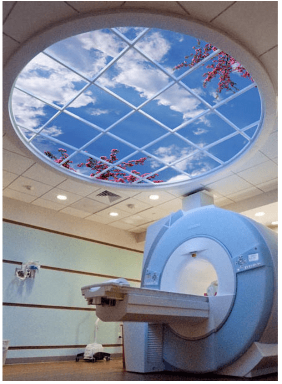 MRI procedure room with a circular window in the ceiling showing a blue sky with a few clouds and flowering tree branches.