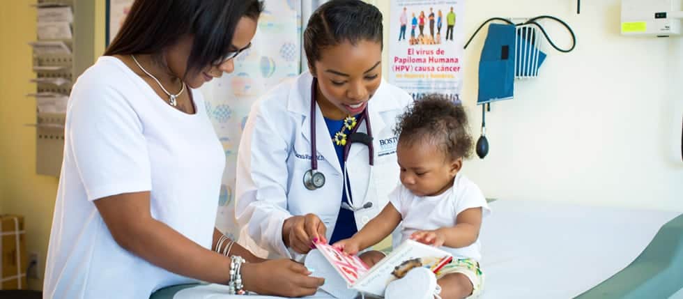 Pediatrician's office showing a doctor and mom smiling and sharing a children's book with a baby.