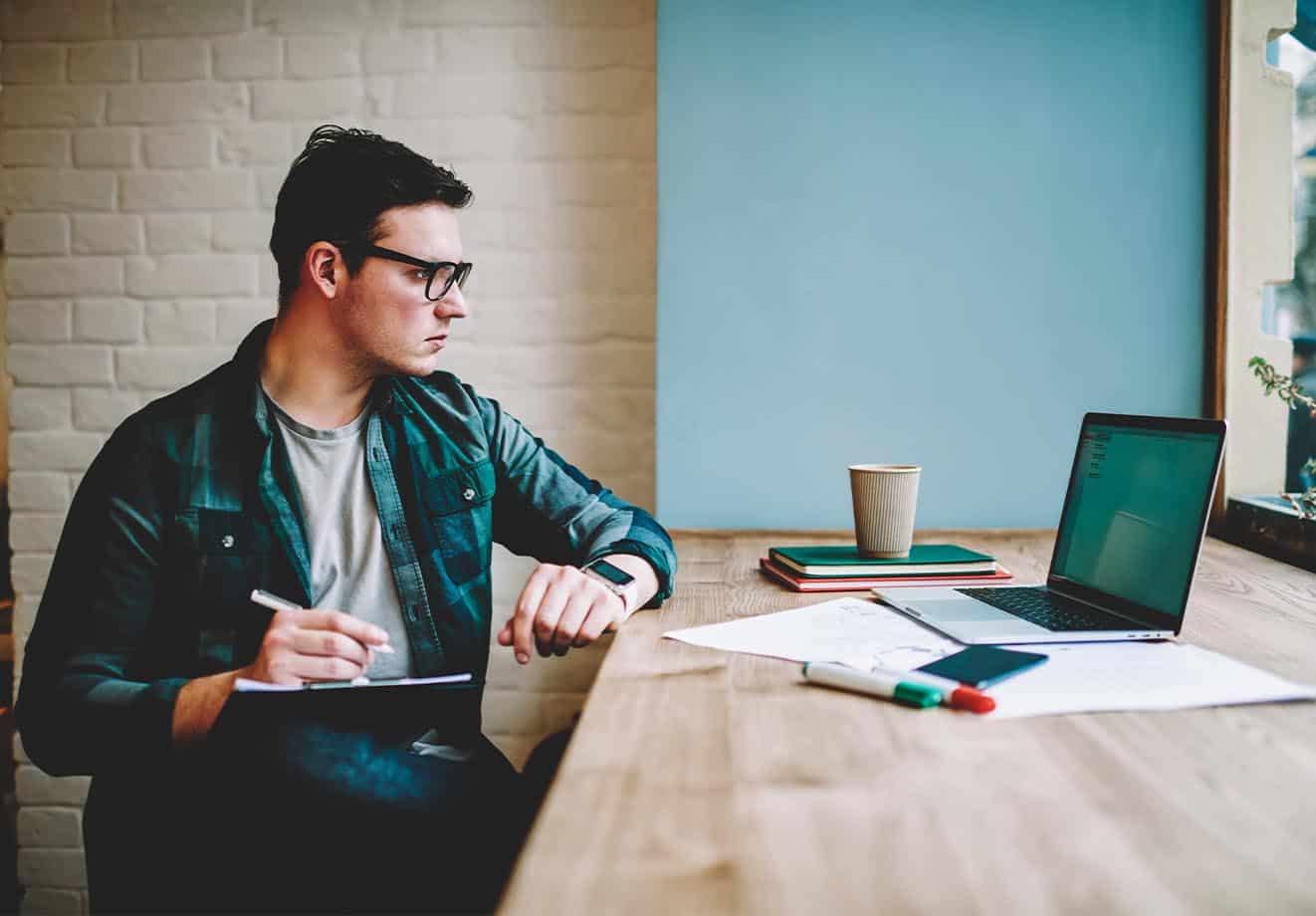 Man writing on a clipboard while looking at a laptop