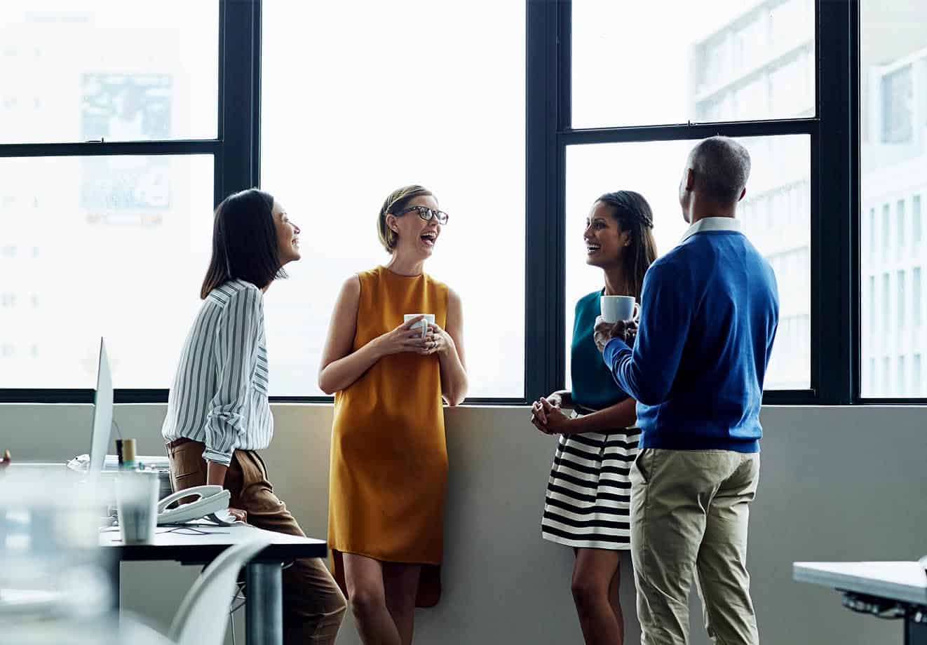 Three women and a man standing and chatting in an office