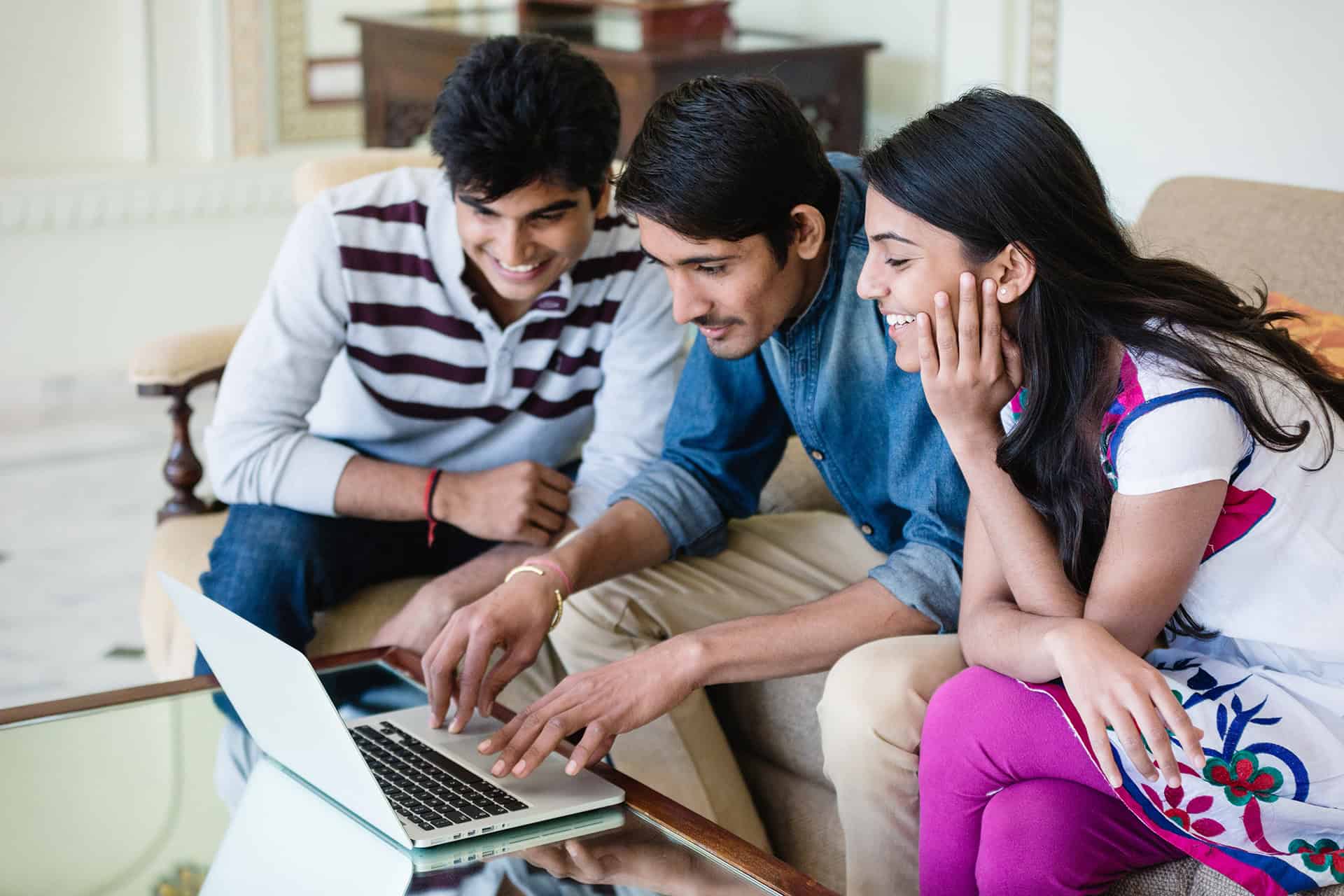 Three people sitting on couch looking at laptop