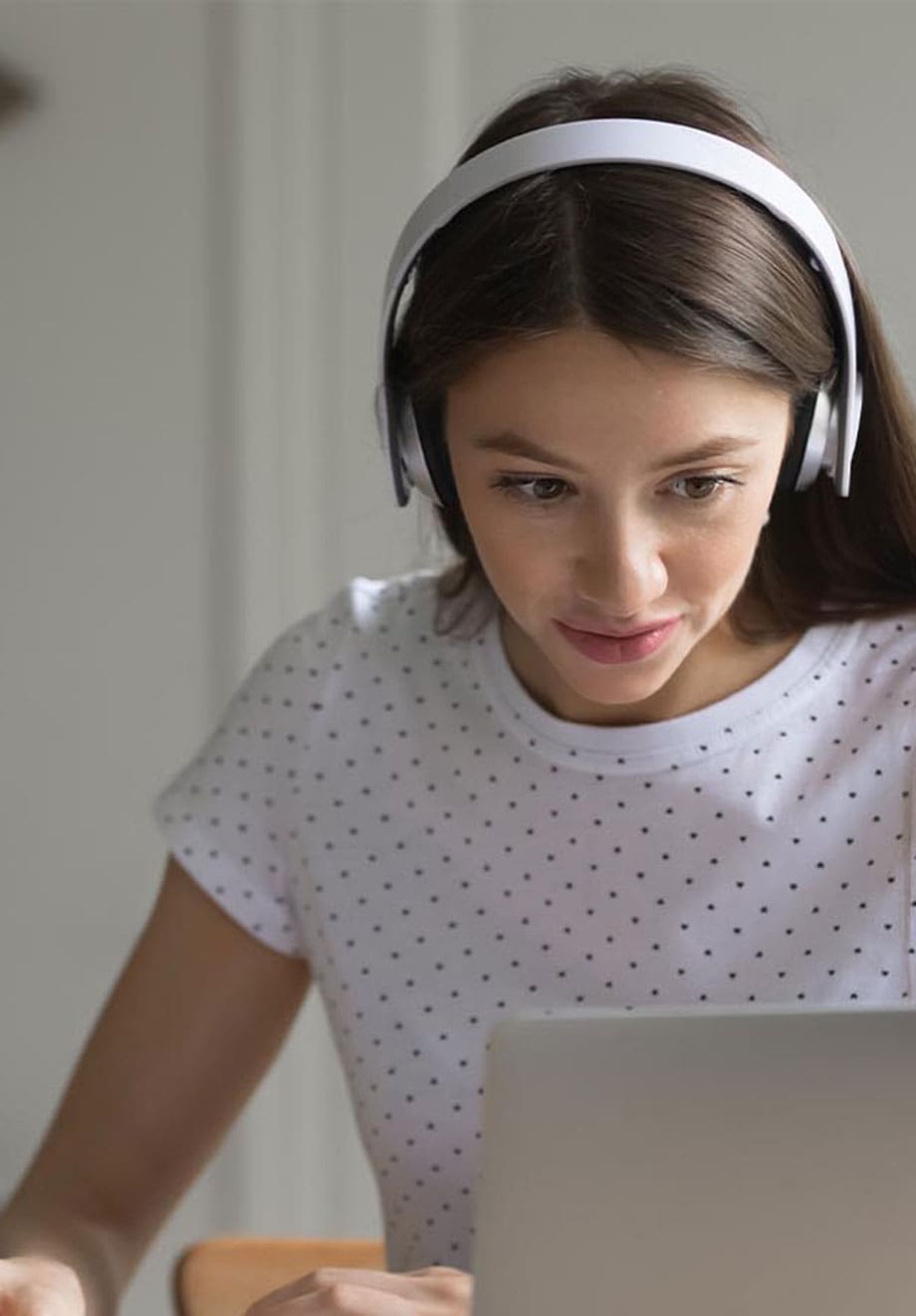 young girl with headphones taking notes off laptop