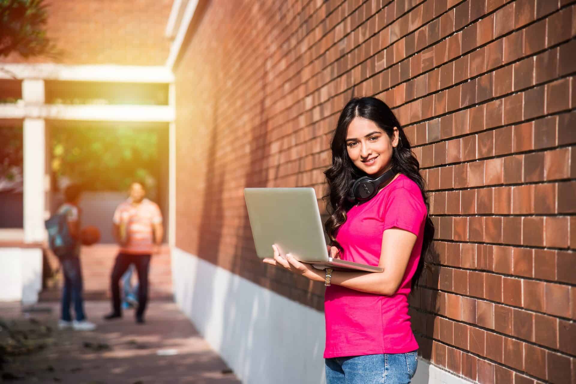 student standing in hallway holding laptop