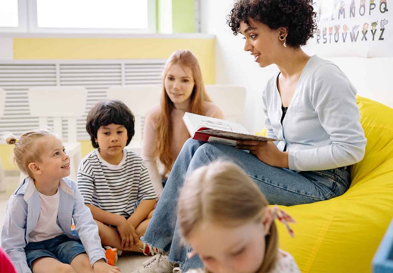 Group of children sitting around their teacher who is reading a book to them