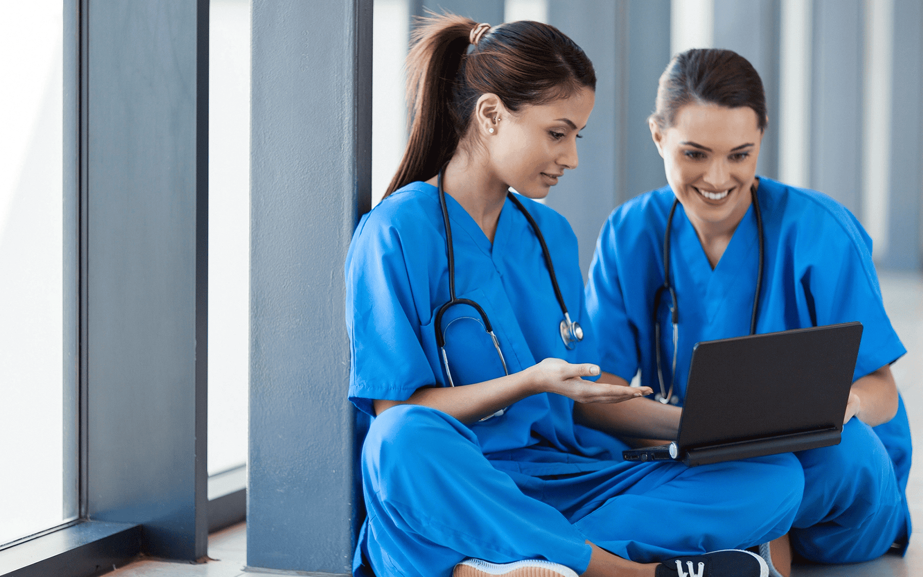 Two nurses sit together using a tablet to access their learning management system