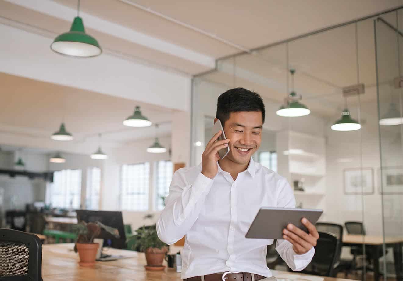 Man in an office talking on a phone while looking at a tablet