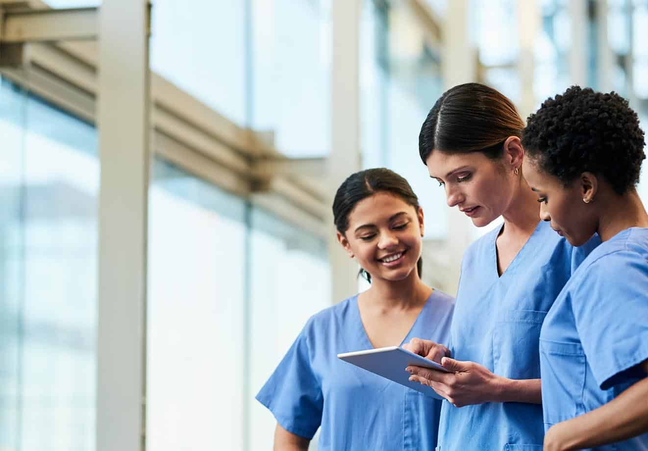 group of three nurses standing together and looking at a tablet