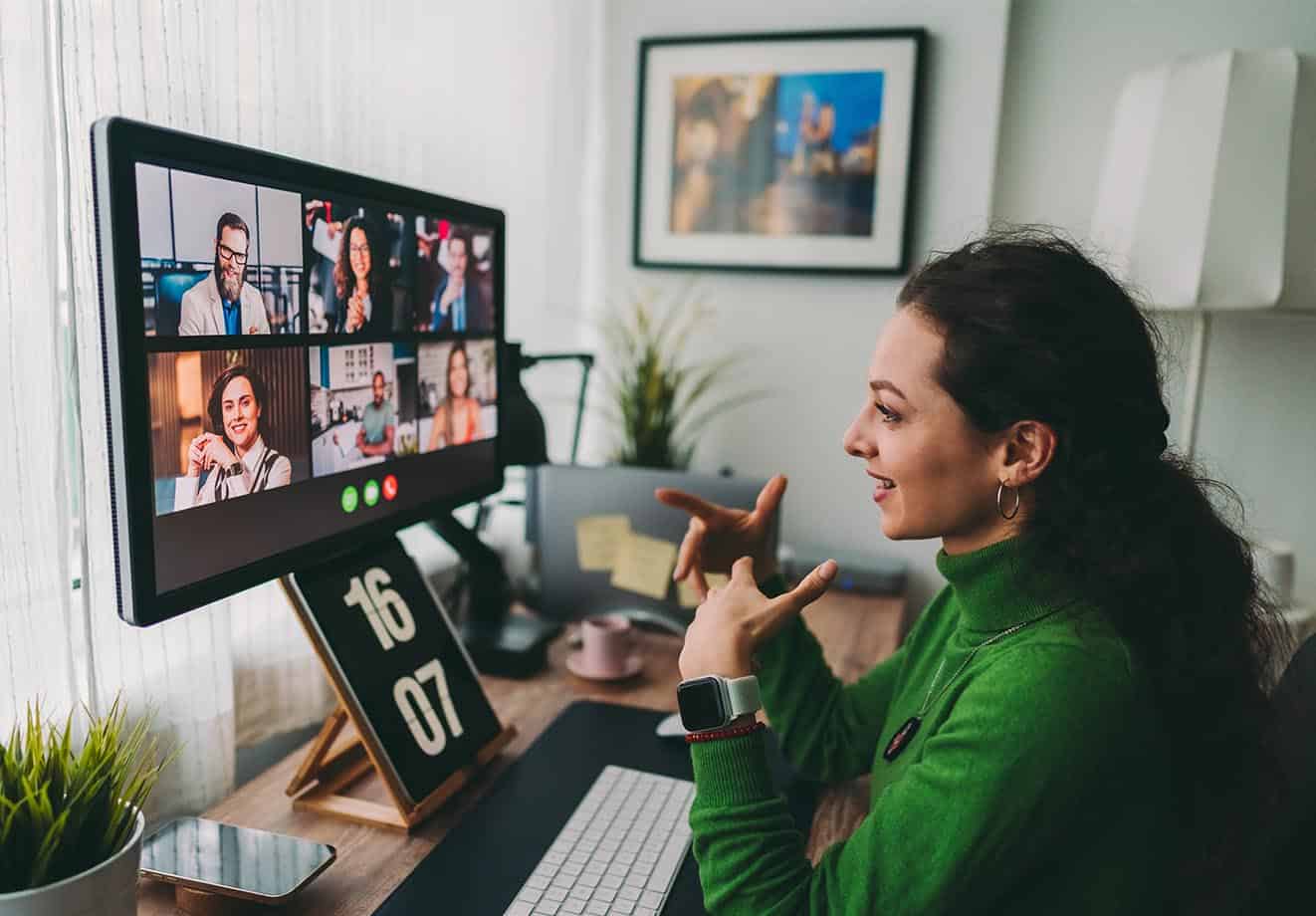 Woman in green sweater speaking to colleagues on her laptop