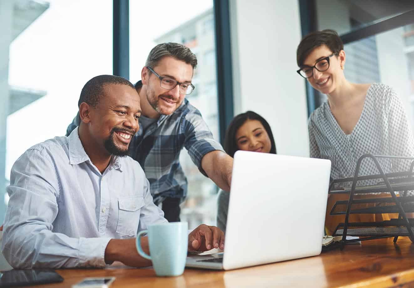 Four people crowd around a laptop screen in a boardroom