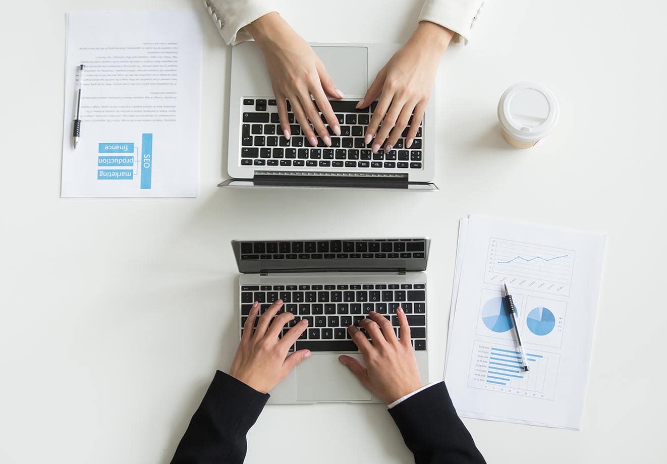 Overhead shot of two laptop keyboards and two sets of hands typing