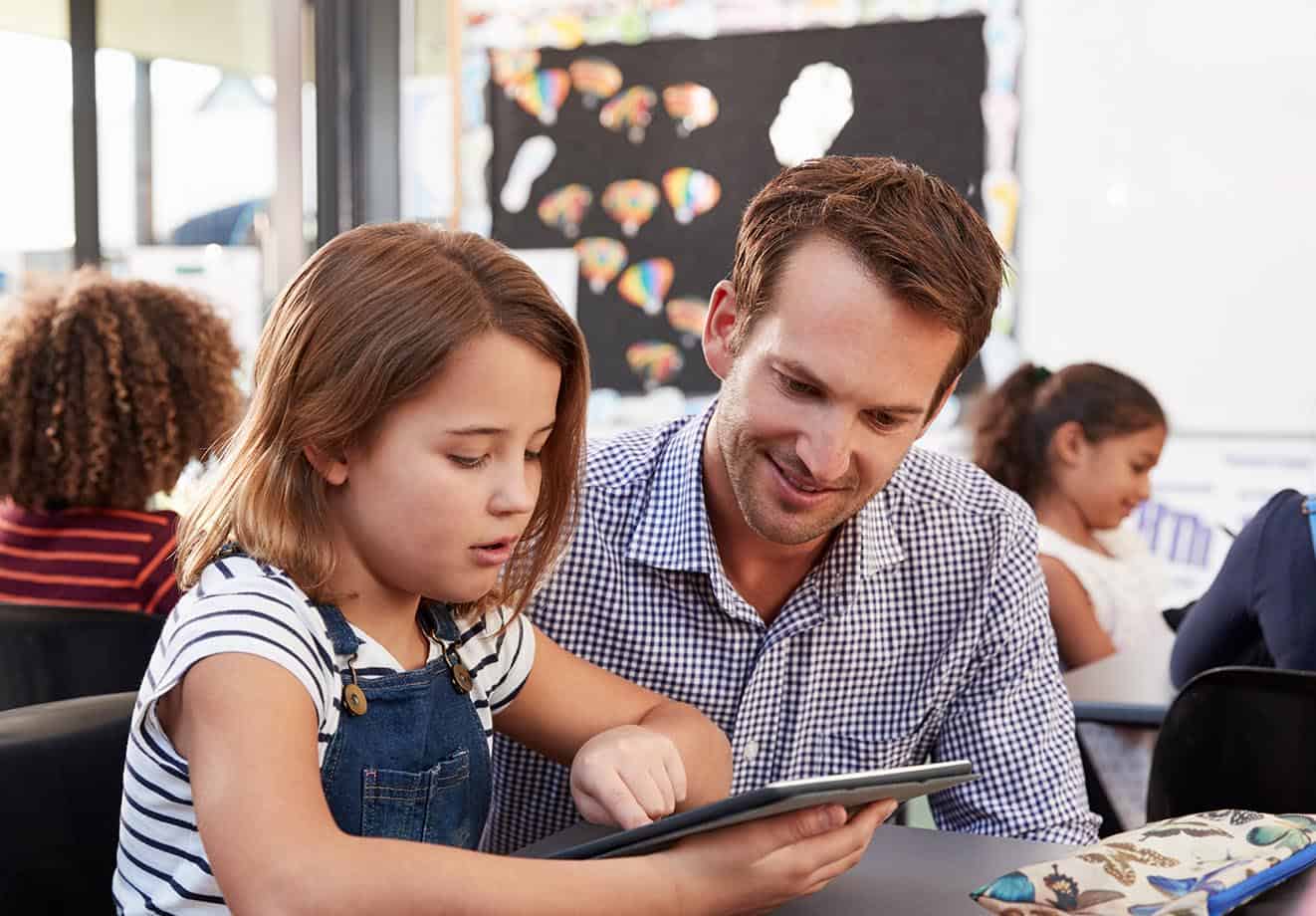 A teacher helping a student on their tablet in a classroom