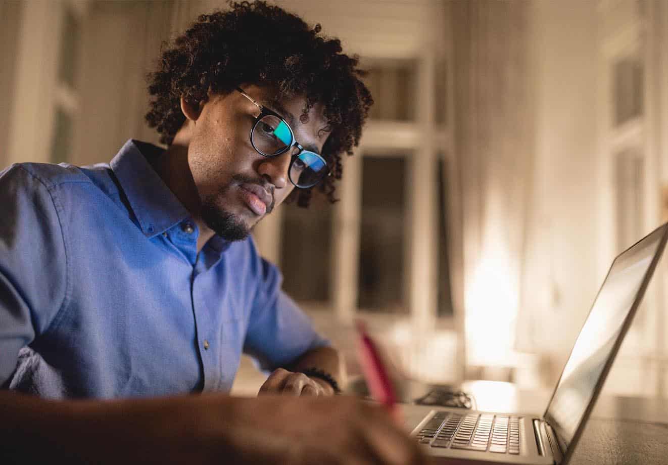 man working on his laptop and writing a note with a red pen