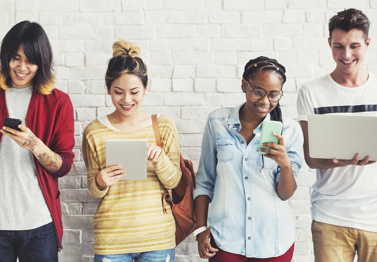 4 students using devices in front of a brick wall