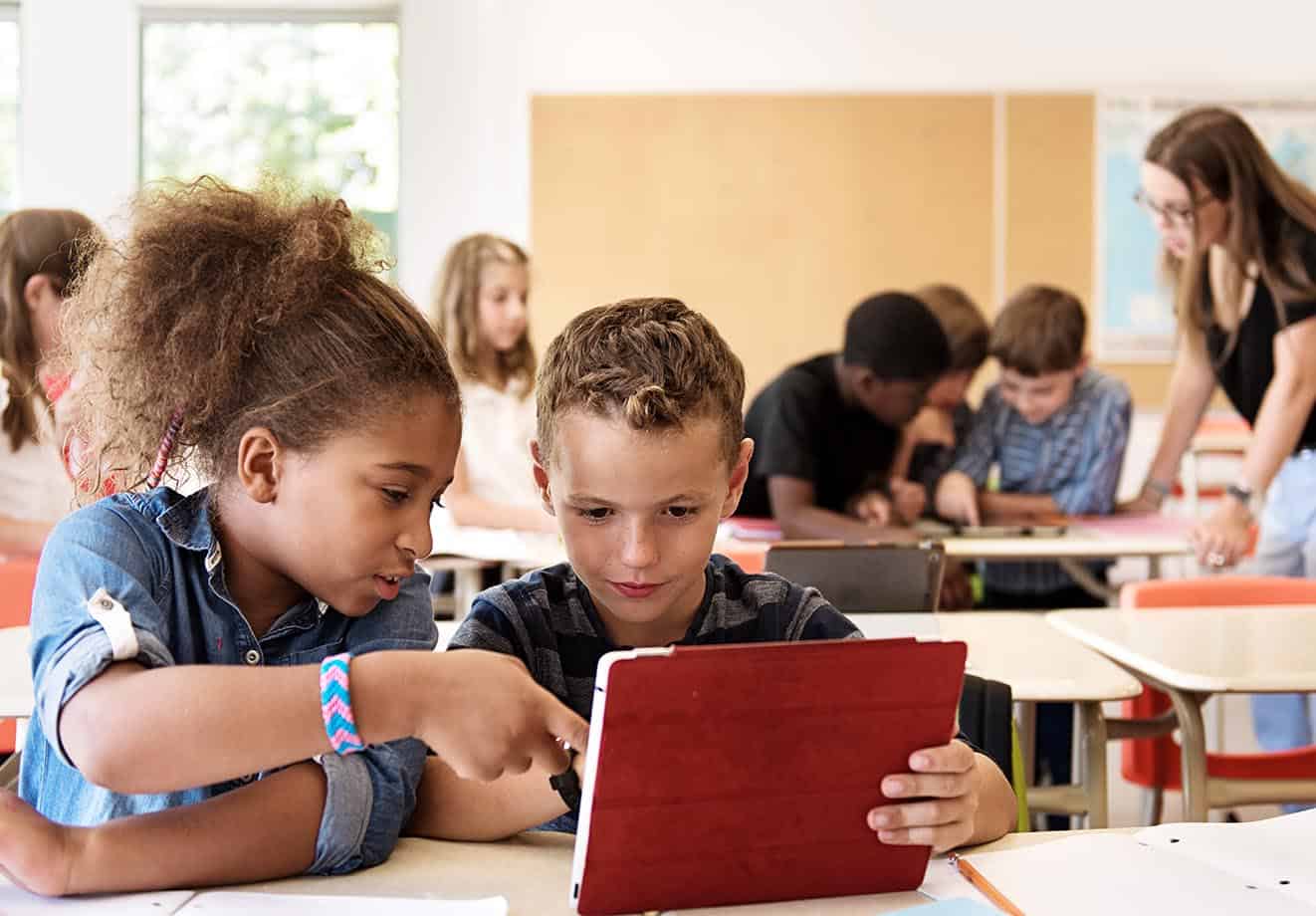 Two children in a classroom working together on a tablet