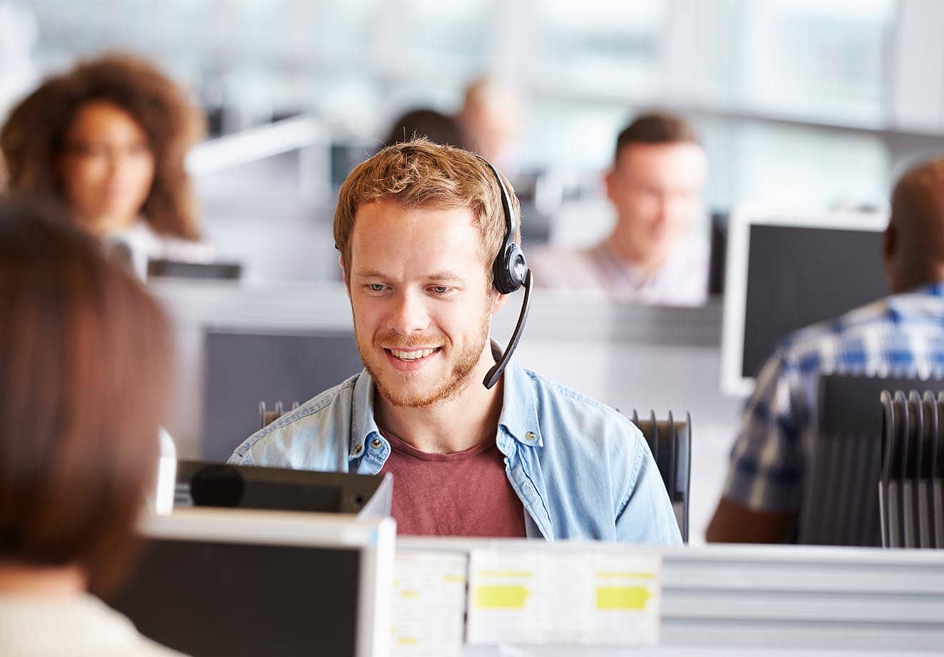 Man wearing a headset and working on a computer in a busy office